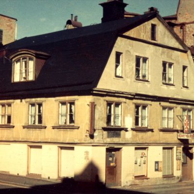 Fotografi på äldre stenhus med en Tobaks och Kortvaruaffär i hörnet av Varvsgatan och Skepparegatan. Kortet är taget någon gång under 1950-talet. Blekinge Museum